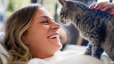 A woman smiling while petting a kitten